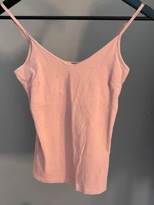 Ljusrosa linnetopp med smala band - Säljer en enkel och stilren ljusrosa linnetopp med smala axelband. Toppen har en rak passform och är tillverkad i mjuk bomull, perfekt för varma dagar eller som layering-piece. Passar dig som gillar minimalistisk och clean stil.