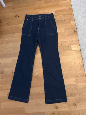 Mörkblå jeans med raka ben från Michael Kors - Snygga mörkblå jeans från Michael Kors med raka ben och stora framfickor. Klassisk femficksmodell med kontrastsömmar och hög midja. Jeansen har en enkel design och är tillverkade i denim. Perfekta för en avslappnad och trendig look. Köpta i USA och aldrig använda. Storlek 8, skulle säga s/m. Säljer då de inte passar mig 