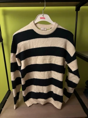 Randig stickad tröja från EDC - Snygg stickad tröja från EDC med breda svarta och beige ränder. Tröjan har rund halsringning och långa ärmar. Perfekt för dig som gillar klassisk men ändå trendig stil. Materialet känns mjukt och bekvämt.