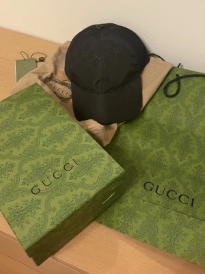 Gucci keps - Snygg svart keps från Gucci med det klassiska GG-monogrammet ton-i-ton över hela kepsen. Kepsen har böjd skärm och justerbar rem bak. Tillverkad i ett glansigt material som ger en exklusiv känsla. Perfekt accessoar för dig som gillar lyxiga detaljer. ALLA TILLBEHÖR MEDFÖLJER ‼️‼️