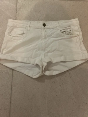 Vita midwaist shorts i bomull - Säljer ett par vita midwaist shorts i mjuk bomull med klassisk femficksdesign och knappstängning framtill. Shortsen har bälteshällor och är perfekta för varma dagar. Snygg och enkel modell som passar till det mesta.