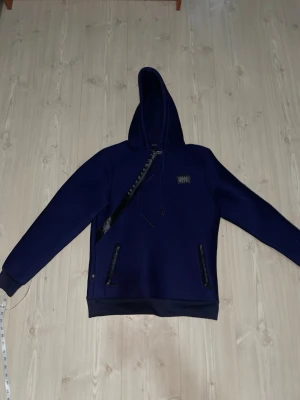Mörkblå hoodie från Philipp Plein - Snygg mörkblå hoodie från Philipp Plein med huva och dragkedjeförsedda fickor. Tillverkad i ett strukturerat material som ger en unik look. Märkespatch på bröstet med Philipp Plein-logga och detaljer i svart. Perfekt för dig som vill sticka ut. Går bra och diskutera priset