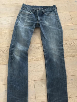 Levi's blå raka jeans - Klassiska blå jeans från Levi's med raka ben och slitna detaljer. Jeansen har fem fickor, knappgylf och tydliga slitningar för en avslappnad look. Tillverkade i denim med en snygg tvättad finish och kontrastsömmar.