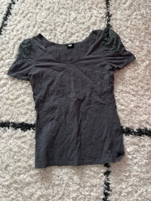 Mörkgrå topp med spetsdetaljer H&M - Snygg mörkgrå topp från H&M med korta ärmar och spetsdetaljer på axlarna. Toppen har en rundad halsringning och är tillverkad i mjuk bomull med dekorativ spets i matchande färg på ärmarna. Perfekt för en trendig och avslappnad look. Vet dock inte vilken storlek tröjan är i men skulle säga att det passar Xs-M! Fick den av min kompis och kommer aldrig till användning 