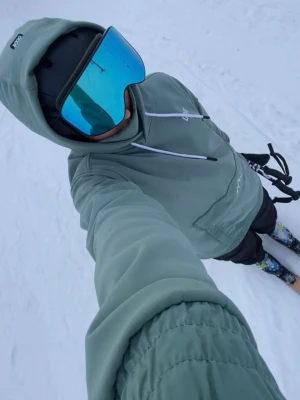 Skidjacka från Dope Snow - Säljer en grön vindjacka från Dope Snow med huva och vita dragsnören. Jackan har två fickor på magen med dragkedjor, samt dragkedja under armhålorna så man kan öppna och lufta om det blir varmt.  Materialet är slitstarkt, vattenavvisande och vindtåligt, perfekt för skid/snowboard åkning. Oversized passform och elastiska muddar.