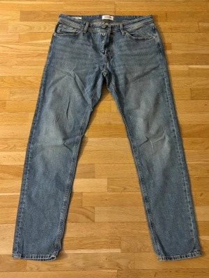 Ljusblå raka jeans - Säljer ett par ljusblå oanvända raka jeans från Jack&Jones med klassisk femficksmodell och knappgylf. Jeansen har en avslappnad passform och har en snygg tvättad look. Perfekta för en casual stil.