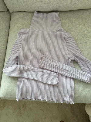 Ljuslila ribbad polotröja Gina Tricot - Ljuslila ribbad polotröja från Gina Tricot. Tröjan har långa ärmar, hög polokrage och är tillverkad i ett mjukt, stretchigt material. Vågig kant nedtill.