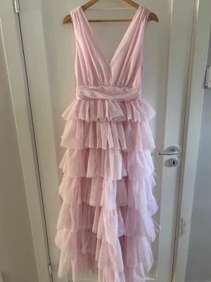 Volangklänning / Balklänning  - Supersöt balklänning i ljusrosa med flera lager volanger och djup v-ringning både fram och bak. Aldrig använd 💕 