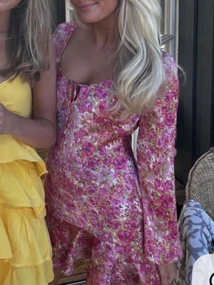 Blommig rosa klänning Zara  - Supersöt klänning i rosa med blommigt mönster från Zara. Klänningen har långa ärmar, djup urringning med snörning framtill och är i ett glansigt material som ger en lyxig känsla, storlek S. Perfekt nu till sommaren!🩷