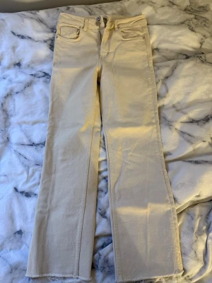Vida beige jeans från Zara - Säljer ett par snygga beige jeans från Zara med raka, vida ben och råa kanter nertill. Jeansen har klassisk femficksdesign och stängs med knapp och dragkedja. Perfekta för en trendig och avslappnad look. Aldrig använt dem. Väldigt korta i längden. 