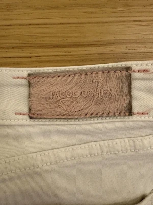  Jacob Cohën jeans - Snygga vita jeans från Jacob Cohën med klassisk femficksmodell och raka ben. Jeansen har diskreta sömmar och patch i ljust läder baktill i midjan. Perfekta för dig som vill ha en clean och stilren look.