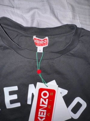 Svart Kenzo t-shirt med tigertryck - Svart t-shirt från Kenzo med ikoniskt tigertryck och texten 'KENZO PARIS' i vitt framtill. Klassisk rund hals och korta ärmar. Tillverkad i mjuk bomull som känns skön mot huden. Perfekt för dig som vill sticka ut med en streetstyle-look. Aldrig använd och helt ny.