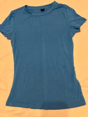 Blå basic t-shirt från SHEIN - En enkel blå t-shirt från SHEIN i storlek S. T-shirten har rund halsringning och korta ärmar. Tillverkad i mjuk bomull, perfekt för en avslappnad och clean look. Passformen är normal och färgen är klarblå.