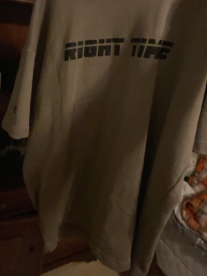 Beige t-shirt med tryck - Säljer en beige t-shirt med svart texten 'RIGHT TIME' över bröstet. T-shirten har en avslappnad passform och korta ärmar. Perfekt för dig som gillar enkel och stilren streetwear.