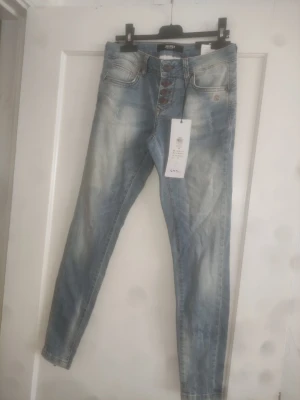 Blå slim fit jeans från  - Snygga ljusblå slim fit jeans från  med slitningar och knappar i gylfen. Jeansen har klassisk femficksdesign, bruna sömmar  Perfekta för en avslappnad och trendig look. Storlek 28 prislapp kvar 699:-