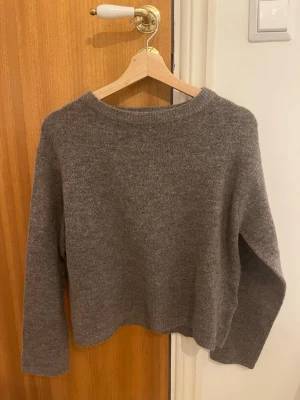 Brun stickad tröja med rund hals - Mysig brun stickad tröja med rund hals och långa ärmar. Tröjan har en enkel och stilren design, perfekt att matcha med jeans eller kjol. Materialet ser ut att vara mjukt och skönt, passar bra för kyligare dagar.