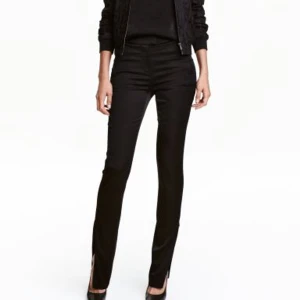 Svarta blanka smala byxor med dragkedjor på benen, i tjockare satin. Strlk: 34. Felfria - Svarta blanka smala byxor med guldfärgad dragkedja längst ner på varje ben, i tjockare satin. Strlk: 34. Knäpps i sidan med dragkedja och knapp. Felfria. Nypris I butik var 399 kr. Första bilden är ett exempel på liknande modell och passform.