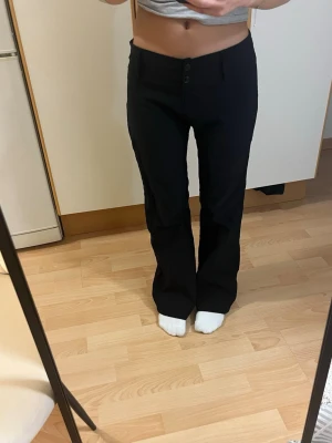 Svarta lågmidjade bootcut kostymbyxor vintage - Säljer ett par svarta kostymbyxor med bootcut-modell och låg midja. Byxorna har två knappar framtill och är i ett skönt, mjukt, stretchigt material som sitter snyggt på kroppen. Okänt märke då de är köpta på vintagebutik i Köpenhamn. Perfekta för en clean och stilren look.