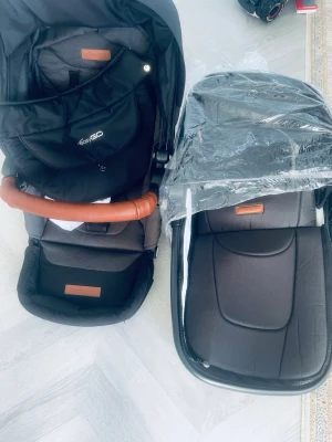 Svart barnvagn med liggdel - Säljer en svart barnvagn från Tosigo med tillhörande liggdel. Vagnen har detaljer i brunt konstläder och en praktisk bygel. Liggdelen har ett genomskinligt regnskydd. Perfekt för promenader och utflykter med småbarn.