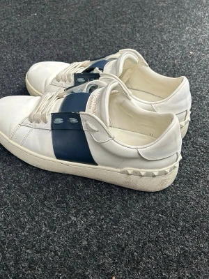 Valentino vita sneakers med blå detalj - Valentino sneakers   Storlek 42.  Mörkblå slinga.  Skick 9/10.  Ritkigt feta passar bra till våren nu.  