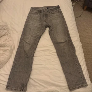 Grå raka jeans från Weekday  - Säljer ett par klassiska grå jeans från Weekday med rak passform. Jeansen har en tidlös look med diskreta sömmar och läderpatch bak i midjan. Perfekta för dig som gillar en enkel och clean stil. Tyvärr finns ett hål i högra fickan 