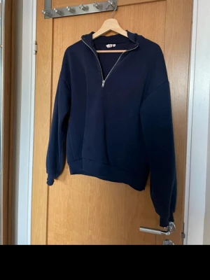 Mörkblå halfzip hoodie från Nelly - Mörkblå hoodie från Nelly med halv dragkedja framtill och ribbade muddar. Oversized passform och mjukt sweatshirtmaterial.