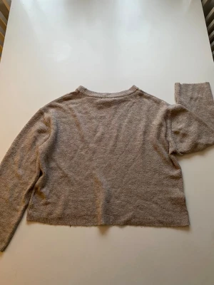 Beige croppad stickad tröja - Mysig beige stickad tröja med croppad passform och långa ärmar. Tröjan har rund halsringning och ribbstickade muddar vid ärmslut och nederkant. Perfekt för lager-på-lager och enkel att matcha med jeans eller kjol.