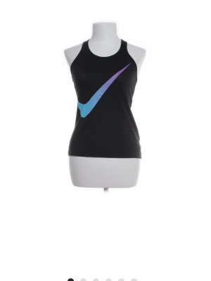 Svart Nike linne med blå logga - Svart linne från Nike med en stor blå och lila swoosh-logga framtill. Sportig modell med brottarrygg och tight passform, perfekt för träning eller en aktiv vardag. Tillverkat i mjukt och stretchigt material för maximal komfort.