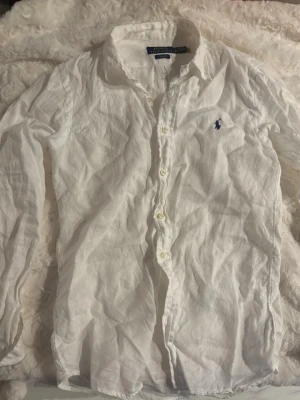 Vit linneskjorta från Polo Ralph Lauren - Vit skjorta i linne från Polo Ralph Lauren. Skjortan har lång ärm, knappar framtill och är slim-fit. Fett laidback till sommaren. Säljer då åt min bror som har växt ur den, använd fåtal gånger.