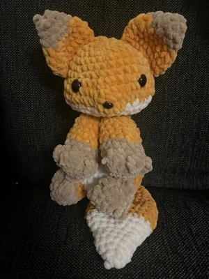 Handgjord virkad räv  - Supergullig handgjord räv i mjuk plysch med orange, grå och vit färg. Räven har stora öron, svans och svarta plastögon. Perfekt som dekoration eller gosedjur. Materialet är fluffigt och känns skönt att hålla i.