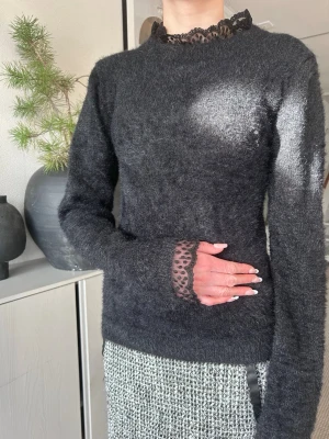 Svart stickad tröja med spetsdetaljer - Mysig och mjuk stickad tröja med lång ärm och fina spetsdetaljer vid halsringning och ärmslut. Tröjan är relativt tunn så den blir inte för varm och ser festlig ut. Lite lyster i tyget. Helt ny och för mig var den för liten (så dottern fick agera modell) 