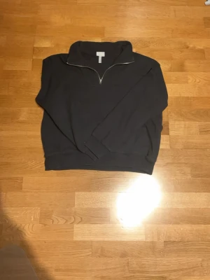 Svart quarterzip hoodie från H&M - Svart hoodie från H&M med quarterzip och hög krage. Tröjan har långa ärmar, ribbade muddar och är tillverkad i mjukt bomullsmaterial. Perfekt för en avslappnad och stilren look. Passar bra nu till våren när det börjar bli varmare.