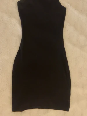 Svart ribbad kort klänning - Snygg svart ribbad klänning med tunna axelband och figurnära passform. Perfekt för dig som gillar minimalistisk stil och vill ha en enkel men trendig look. Klänningen är kort och har en stilren design som passar till många tillfällen.