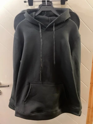 Svart hoodie - Det Stilren svart hoodie oanvänd i medium fit tillverkad av 100% polyester för hög komfort och hållbarhet. Mjuk, lätt och behåller passformen tvätt efter tvätt. Perfekt för både vardag och fritid.🌟