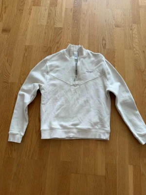 Vit halfzip hoodie Axel Arigato - Snygg vit hoodie från Axel Arigato med halfzip och hög krage. Tröjan har ett diskret tryck på bröstet och ribbade muddar vid ärmslut och midja. Perfekt för en clean och stilren look.