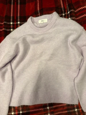 Ljuslila stickad tröja Gina Tricot - Mysig ljuslila stickad tröja från Gina Tricot i ullblandning. Tröjan har rund halsringning, ribbade muddar och en avslappnad passform. Perfekt för att hålla värmen under kyliga dagar. Tyvärr har den ett hål i ryggen som jag har försökt sytt igen men det var ganska svårt, så jag säljer denna till någon som kanske vill ha den och kan sticka eller sy igen den bättre. Köpte den 7/2-2026, har inte hunnit använt den då den gick sönder och jag kan ej reklamera den. Annars är tröjan så fin i färgen.