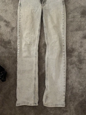 Grå mid wide jeans med raka ben - Säljer ett par ljusgrå jeans med midja i modellen mid wide, raka ben och längd 32. Jeansen har klassisk femficksdesign och dragkedja. Perfekta för en avslappnad och trendig look.