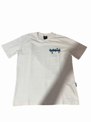 Vit t-shirt från Hoodrich med tryck - Säljer en vit t-shirt från Hoodrich i storlek M. T-shirten har ett blått och svart grafiskt tryck med texten 'Hoodrich' och stjärnor på bröstet. Klassisk rund hals och korta ärmar. Tillverkad i mjuk bomull för skön känsla.