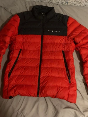Röd och svart pufferjacka Sail Racing - Snygg röd och svart pufferjacka från Sail Racing med hög krage och två dragkedjeförsedda fickor. Perfekt för kommande vårdagar och riktigt skön att bära. Jackan är i ett mycket fint skick och är använd med hänsyn. Enda defekten är att sömmen gått upp lite i kragen högst upp på jackan (sista bilden) men inget man märker av alls! Jackan är köpt för 2 år sedan så minns inte helt vad den kostade men ~~ 3000 kr Hör gärna av er om minsta lilla! OBS Jackan passar dig som är 170-180 beroende på vikt.