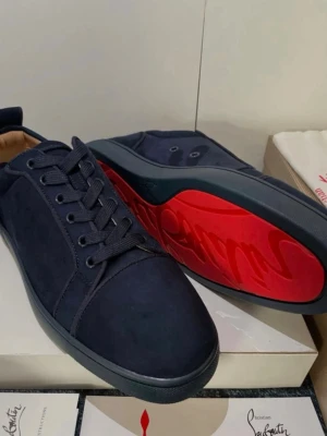Mörkblå sneakers från Louboutin - Snygga mörkblå sneakers från Christian Louboutin med klassisk låg profil och ikonisk röd sula. Skorna är gjorda i mocka med matchande mörkblå snörning och diskreta detaljer. Perfekt för dig som vill sticka ut med exklusiv design och lyxig känsla.