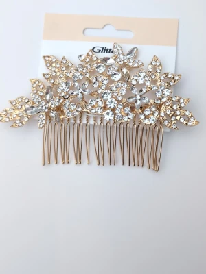 Guldig hårkam med strass från Glitter - Superfin hårkam i guldmetall dekorerad med gnistrande strass i blommönster. Perfekt för att ge frisyren extra bling och en lyxig känsla. Blommorna och bladen är täckta av klara stenar som fångar ljuset snyggt. Snygg accessoar för dig som vill sticka ut.