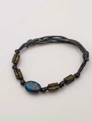 Svart armband med blå pärla - Snyggt armband med svart justerbart band, dekorerat med en blåmönstrad oval pärla i mitten och antikguld-färgade metallpärlor. Perfekt accessoar för en cool och avslappnad stil.