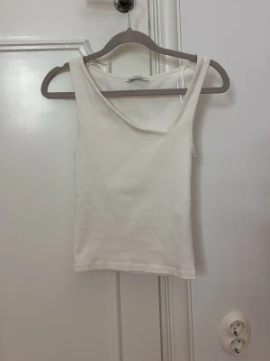 Vit ärmlös linnetopp - En enkel och stilren vit linnetopp med rund halsringning. Toppen är ärmlös och har en rak passform, perfekt att matcha med jeans eller kjol. Tillverkad i mjukt bomullsmaterial för en bekväm känsla.