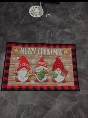 Julmatta Merry Christmas tomtar - Färgglad julmatta med tre söta tomtar, texten 'Merry Christmas' och röd-svart rutmönstrad kant. Mattan har motiv av tomtar med julklappar, pepparkaka och polkagris. Tillverkad i syntetmaterial, perfekt som dekoration till julen.  Finns fler jul saker på min sida