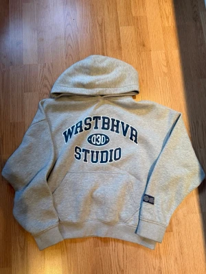 Grå WRSTBHVR hoodie - Snygg grå hoodie från WRSTBHVR Studio med mörkblå tryck på bröstet. Storleken är small men passar även medium. Väldigt bekväm och mjuk i materialet, perfekt både till vardags och som en avslappnad streetwear-look. Passar perfekt till både jeans och mjukisar. Färgen är en ljus grå som är lätt att matcha med det mesta. I fint skick och använd få gånger. Pris kan diskuteras 