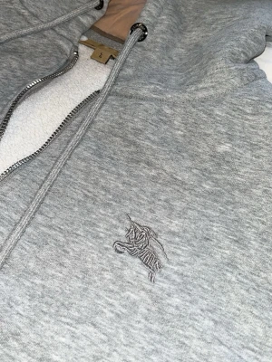 Grå zip-hoodie från Burberry - Säljer min burburry zip hoodie använt hyfsat lite fof väldigt fräsch tröja inga slitningar . Perfekt för dig som vill ha en stilren hoodie med lyxig känsla och fett mönster.