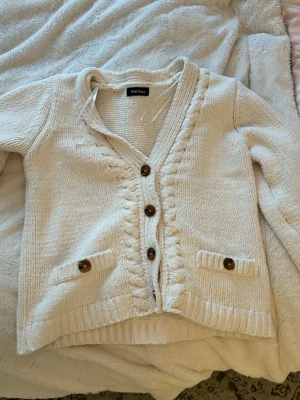 Kofta  - Stickad cremevit kofta med bruna knappar och använd 2 gånger