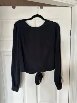 Svart blus med djup rygg - Säljer denna superfina blusen från Nelly med öppen rygg och knytdetalj bak. Toppen är i nyskick och storlek 38💘 