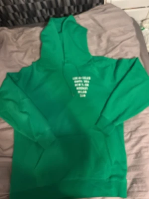 Grön hoodie med vita stadnamn - Snygg grön hoodie med huva och dragsnören. På bröstet finns vita tryckta stadnamn som Los Angeles, Yokohama, New York, London, Milan och NYC. Tillverkad i mjukt sweatshirtmaterial som känns skönt mot huden. Perfekt för dig som gillar streetwear och enkel stil.