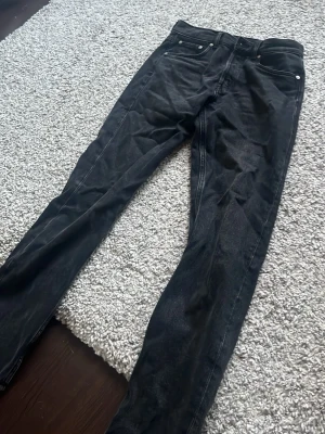 Svarta jeans med fem fickor, passform straight leg. - Säljer ett par svarta straight leg jeans med klassisk femficksdesign och bra passform. Jeansen har svarta sömmar och silverfärgade nitar vid fickorna. Byxorna används ett fåtal gånger men har legat i garderoben några månader. Passade inte mig längre.